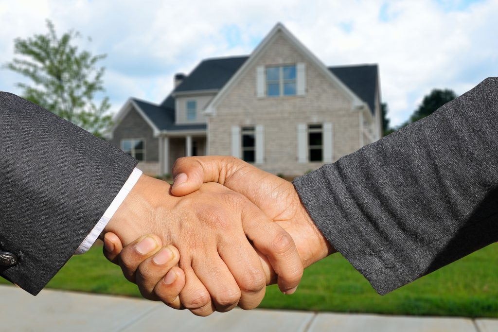 Photo de mains qui se serrent devant une maison